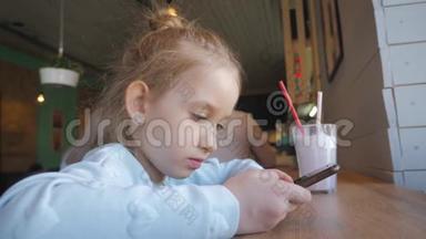 可爱的小女孩在咖啡馆里用智能手机。 快乐的孩子在<strong>放学</strong>后玩得开心和放松。 自然室内